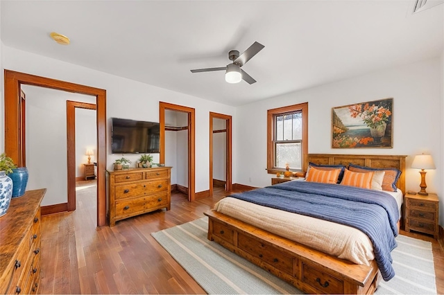 bedroom with visible vents, baseboards, ceiling fan, wood finished floors, and two closets