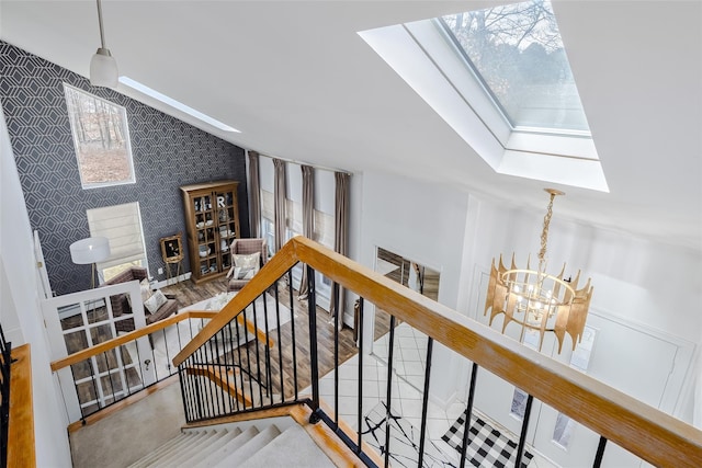 staircase featuring wallpapered walls, vaulted ceiling with skylight, an accent wall, and an inviting chandelier