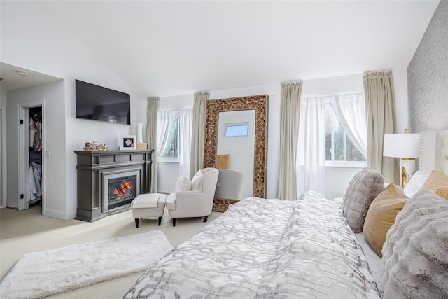 bedroom featuring lofted ceiling, light carpet, and a glass covered fireplace