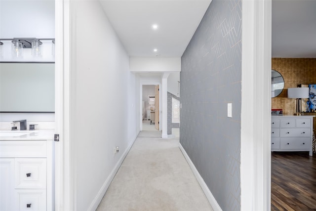 hall featuring carpet floors, baseboards, a sink, and recessed lighting