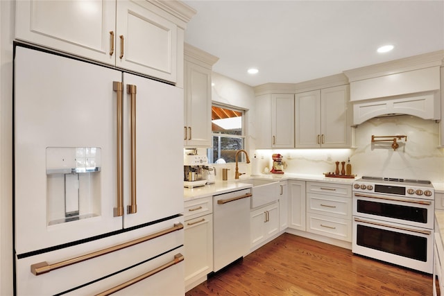 kitchen with premium appliances, light countertops, backsplash, light wood-style flooring, and a sink