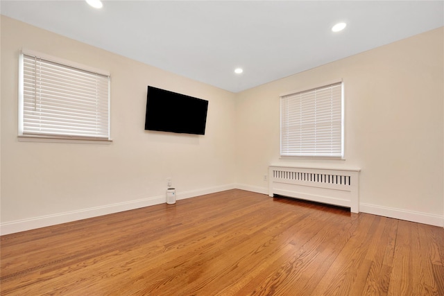 empty room featuring baseboards, light wood finished floors, recessed lighting, and radiator