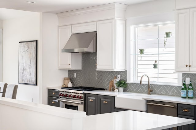 kitchen featuring light countertops, backsplash, appliances with stainless steel finishes, a sink, and ventilation hood