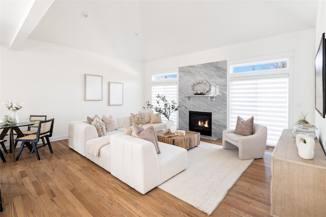 living area with a high ceiling, beamed ceiling, a fireplace, and light wood-style flooring