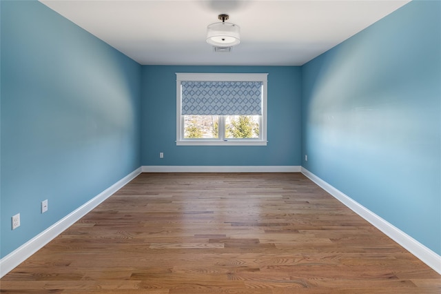 spare room with wood finished floors, visible vents, and baseboards