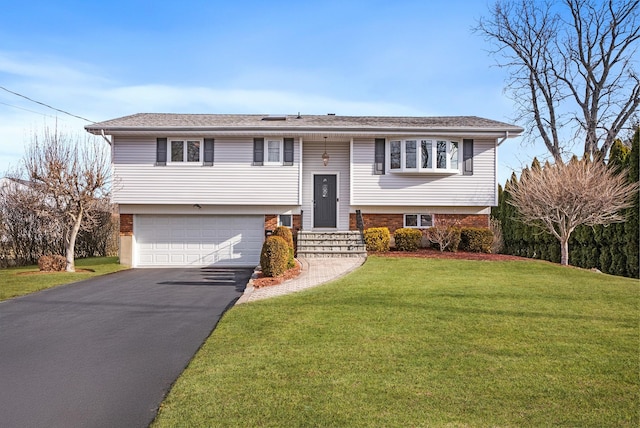 raised ranch featuring aphalt driveway, a front yard, brick siding, and an attached garage