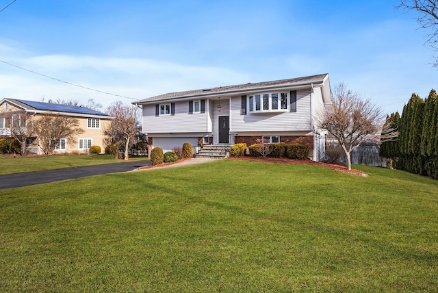 raised ranch featuring an attached garage, brick siding, fence, driveway, and a front yard