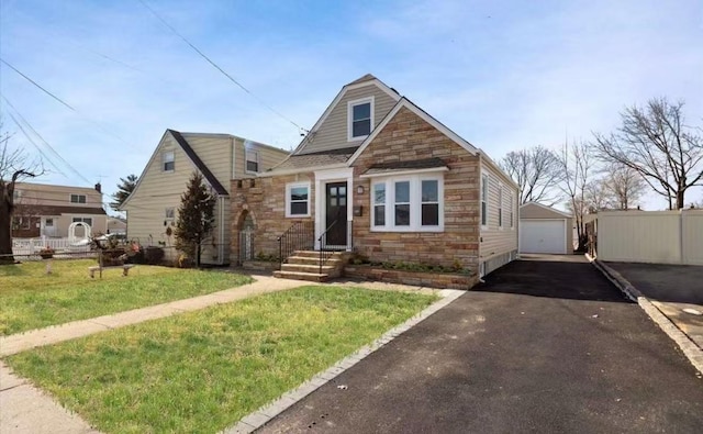 view of front of property with an outbuilding, driveway, stone siding, and fence