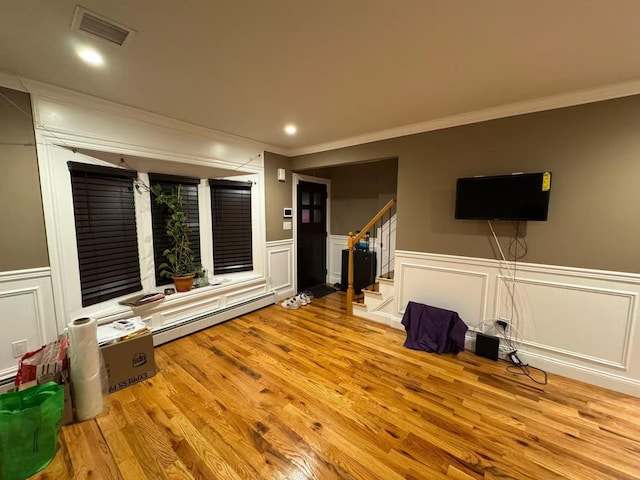 interior space with a wainscoted wall, wood finished floors, visible vents, stairway, and baseboard heating