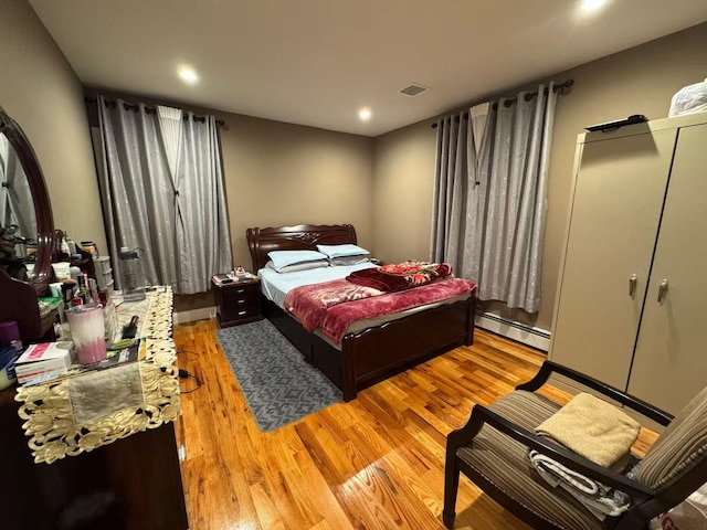 bedroom featuring a baseboard heating unit, visible vents, and light wood-style flooring