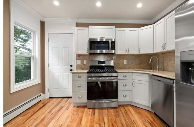 kitchen featuring crown molding, stainless steel appliances, light countertops, baseboard heating, and a sink