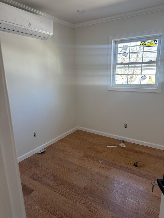 spare room featuring an AC wall unit, crown molding, baseboards, and wood finished floors