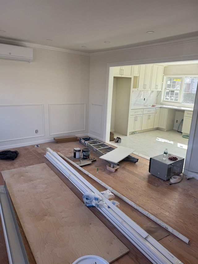 unfurnished dining area with a wall unit AC, a decorative wall, crown molding, and wainscoting