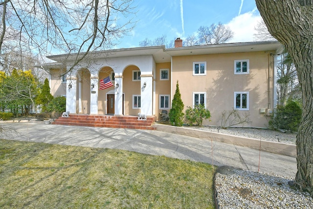 view of front of property with a front yard, a chimney, and stucco siding