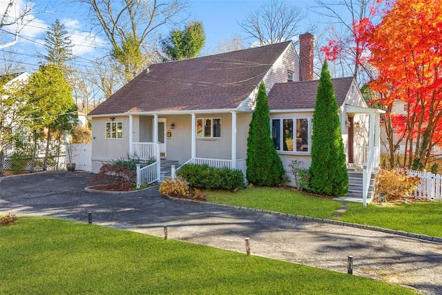 view of front of home featuring stucco siding, a shingled roof, covered porch, a front yard, and fence