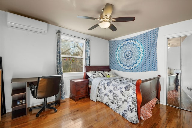 bedroom featuring baseboards, a wall unit AC, wood-type flooring, ceiling fan, and a closet