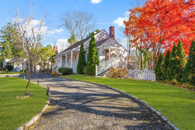 view of property exterior with gravel driveway, a yard, a chimney, covered porch, and fence