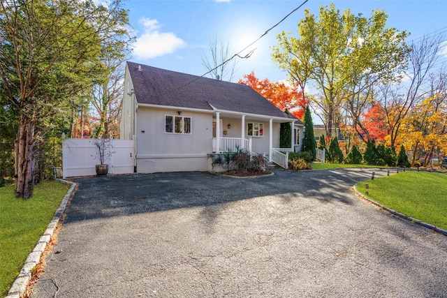 view of front of home featuring covered porch, roof with shingles, aphalt driveway, and a front lawn