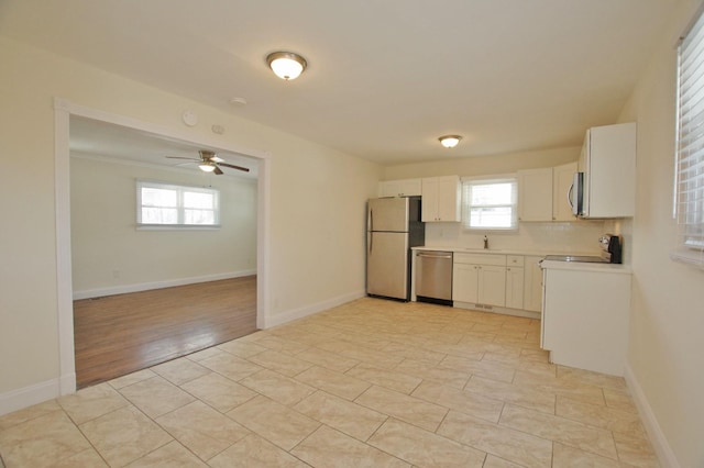 kitchen with stainless steel appliances, light countertops, white cabinets, a sink, and baseboards