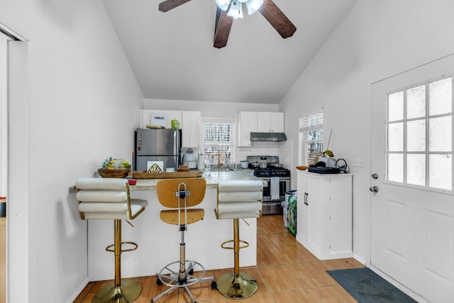 kitchen featuring white cabinets, lofted ceiling, appliances with stainless steel finishes, under cabinet range hood, and a kitchen bar