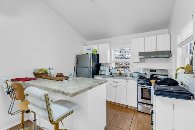 kitchen featuring stainless steel appliances, light countertops, white cabinetry, under cabinet range hood, and a kitchen breakfast bar