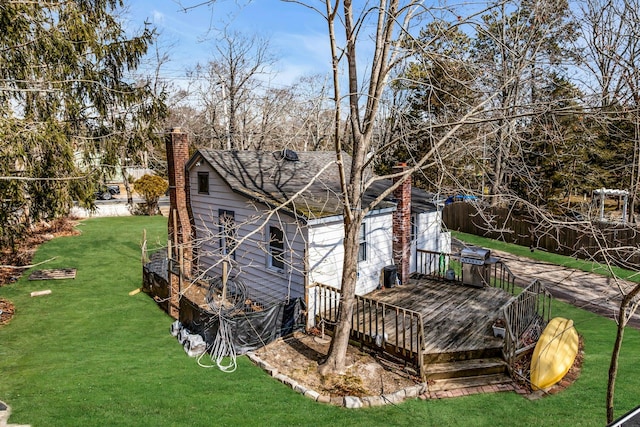 back of property with a deck, a shingled roof, a lawn, and a chimney