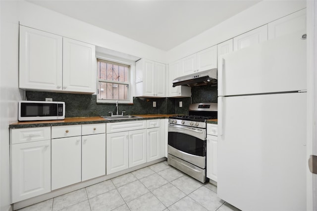 kitchen featuring dark countertops, white cabinetry, a sink, white appliances, and under cabinet range hood