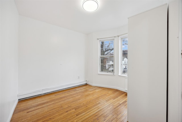 empty room featuring light wood finished floors, a baseboard radiator, and baseboards