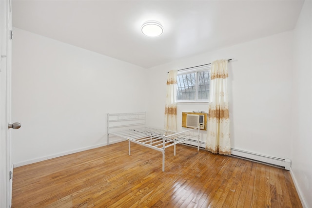 interior space with a baseboard radiator, a wall mounted air conditioner, baseboards, and hardwood / wood-style floors