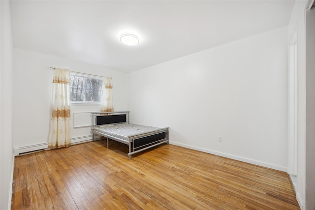 unfurnished bedroom featuring a baseboard heating unit, baseboards, and hardwood / wood-style floors