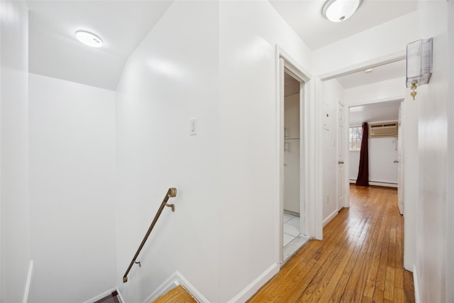 hall with light wood-style flooring, an upstairs landing, and baseboards