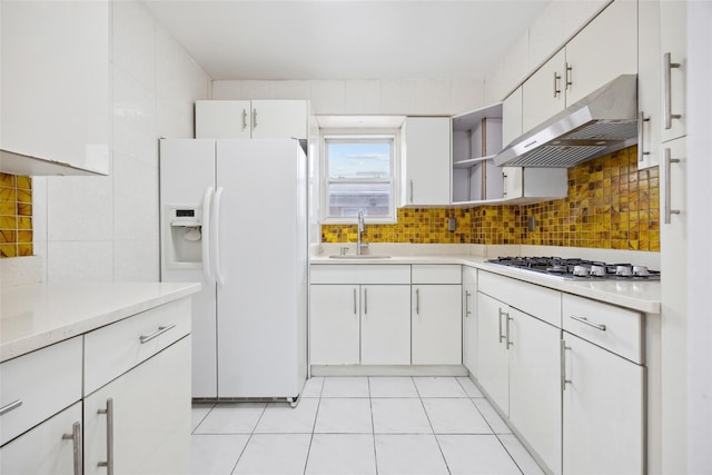 kitchen with white refrigerator with ice dispenser, stainless steel gas stovetop, decorative backsplash, a sink, and under cabinet range hood