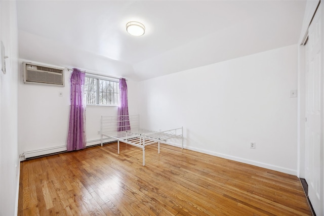 unfurnished room with a baseboard radiator, baseboards, vaulted ceiling, an AC wall unit, and hardwood / wood-style floors