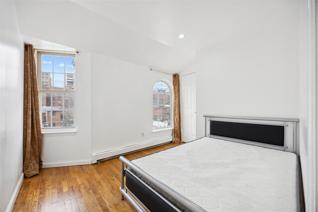 bedroom featuring light wood finished floors, a baseboard radiator, multiple windows, and vaulted ceiling