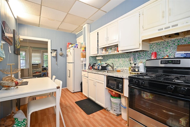 kitchen with black microwave, under cabinet range hood, a sink, stainless steel range with gas cooktop, and freestanding refrigerator