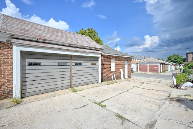 view of side of property featuring a garage, an outbuilding, brick siding, and a shingled roof