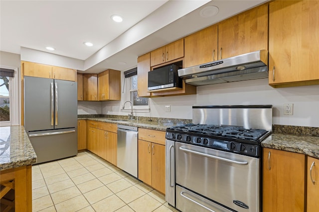 kitchen featuring light tile patterned floors, under cabinet range hood, stainless steel appliances, a sink, and dark stone counters