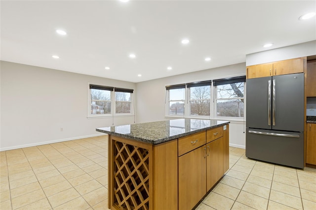 kitchen with light tile patterned floors, recessed lighting, a kitchen island, freestanding refrigerator, and dark stone countertops