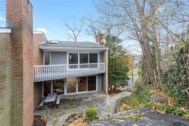 back of property with a patio, a shingled roof, and a chimney