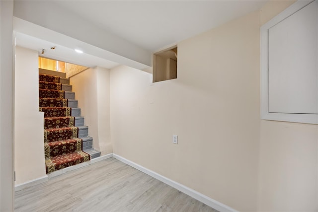 finished basement with stairway, light wood-style flooring, and baseboards