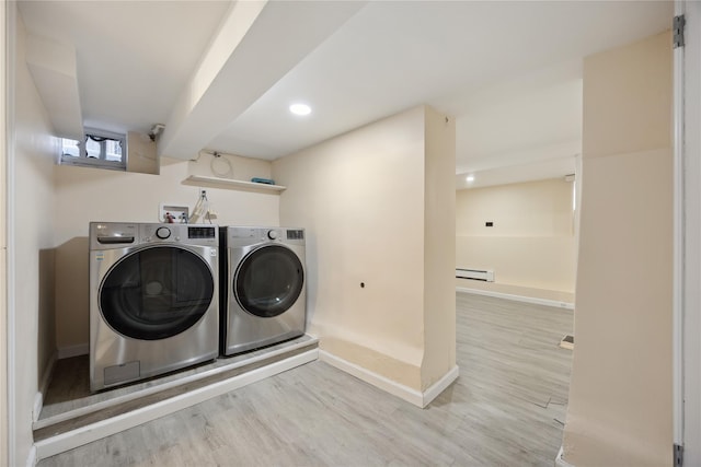 clothes washing area with baseboards, a baseboard radiator, laundry area, wood finished floors, and washer and clothes dryer