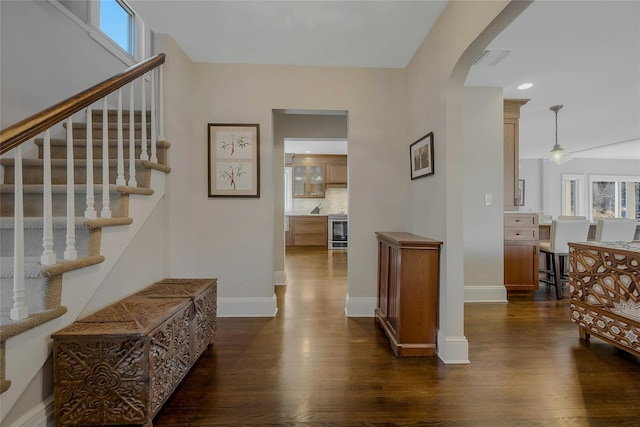 entryway with arched walkways, visible vents, baseboards, stairway, and dark wood finished floors