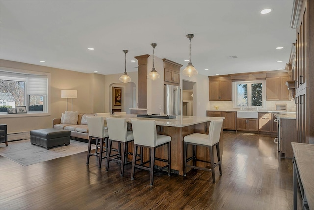 kitchen with arched walkways, dark wood finished floors, recessed lighting, stainless steel fridge, and a kitchen bar