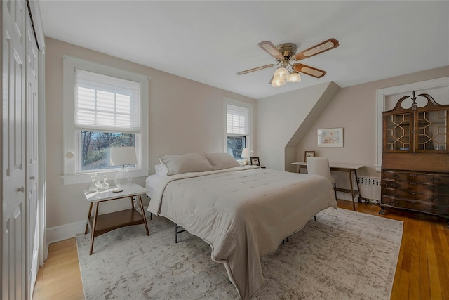 bedroom with light wood-type flooring, radiator, baseboards, and ceiling fan