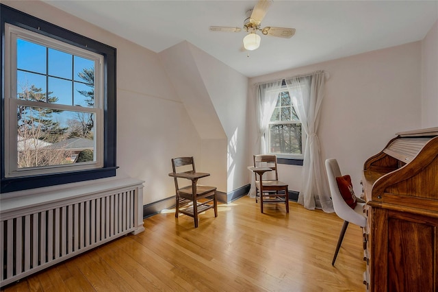 sitting room featuring ceiling fan, light wood finished floors, baseboards, and radiator