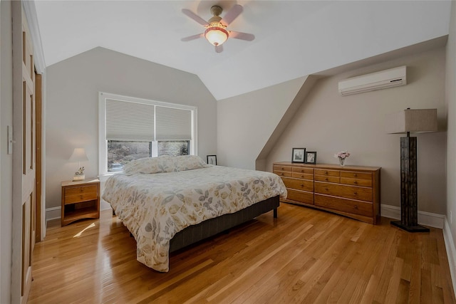 bedroom with light wood-type flooring, an AC wall unit, vaulted ceiling, and baseboards