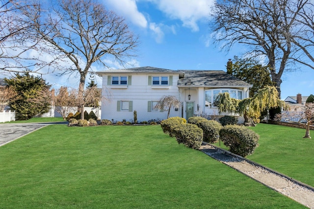 tri-level home with aphalt driveway, fence, and a front lawn