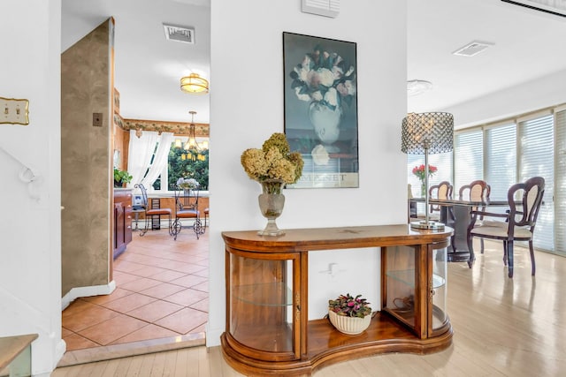 hall with baseboards, visible vents, a chandelier, and wood finished floors