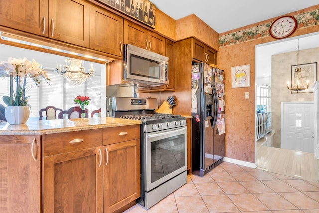 kitchen featuring brown cabinets, a notable chandelier, light tile patterned floors, hanging light fixtures, and appliances with stainless steel finishes