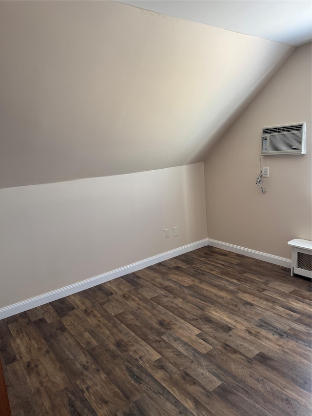 bonus room featuring a wall unit AC, radiator, dark wood-type flooring, vaulted ceiling, and baseboards